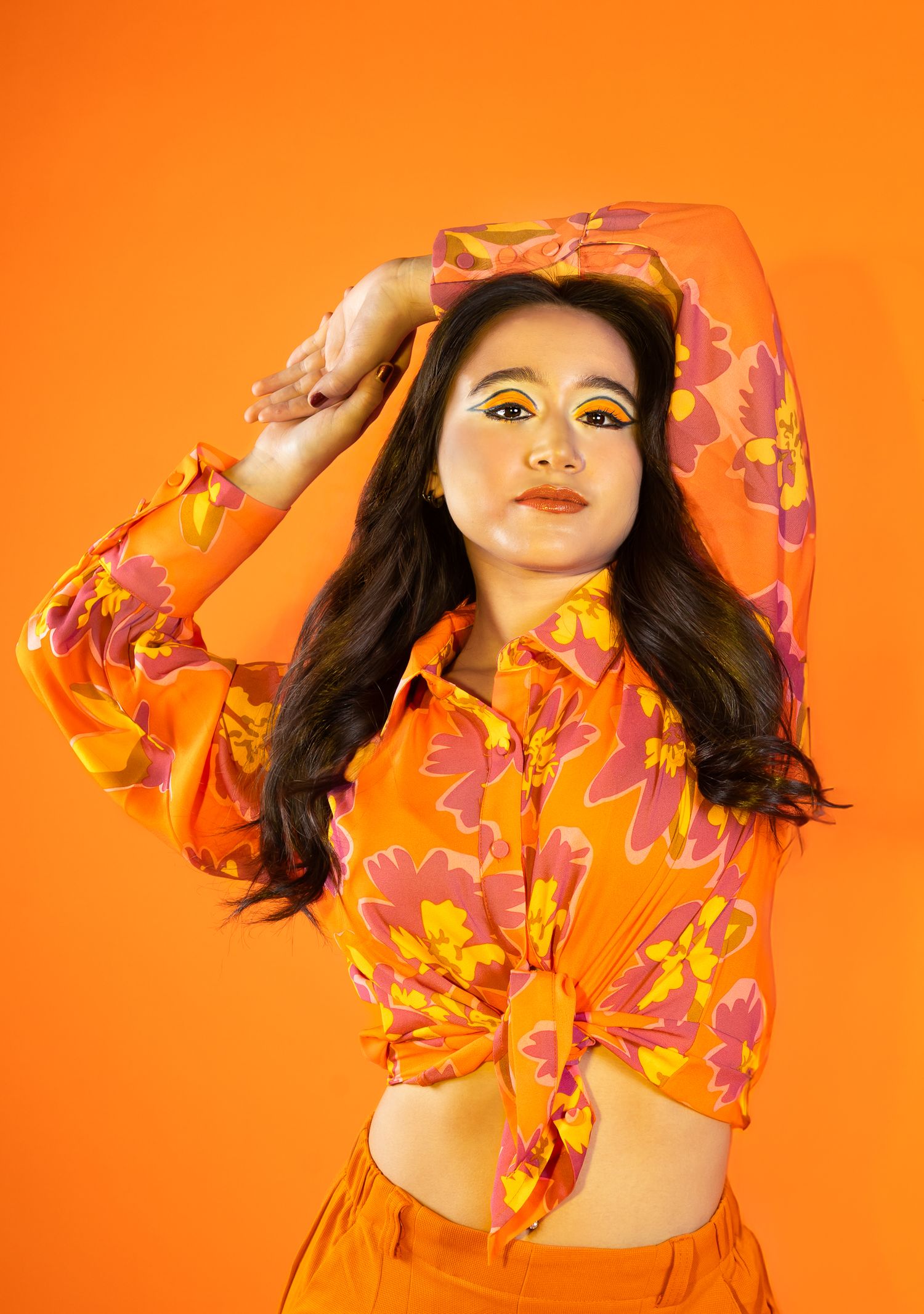 Girl posing in all orange and orange backdrop, arms in the air