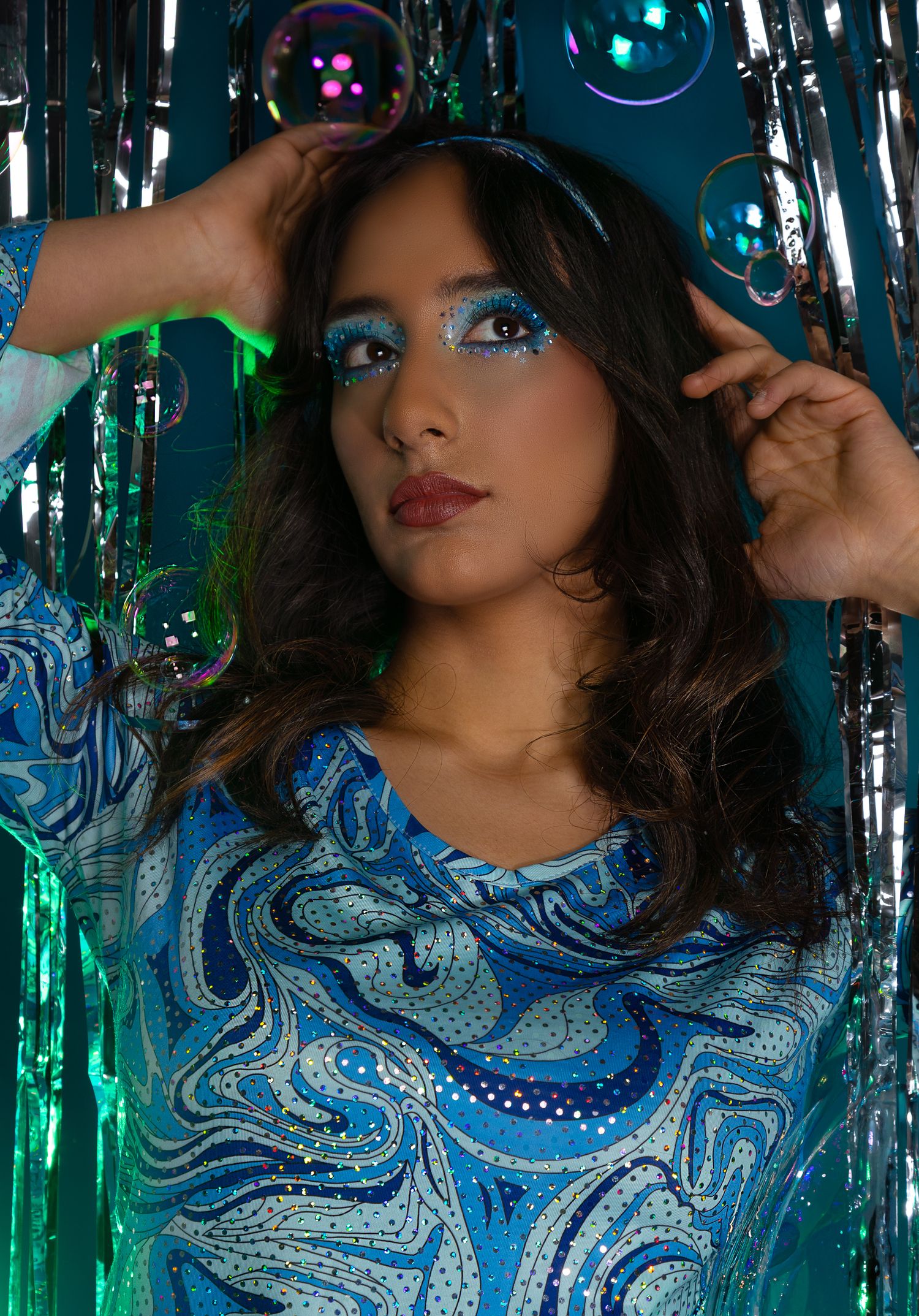Girl posing in front of a disco style backdrop with bubbles, hands in the air