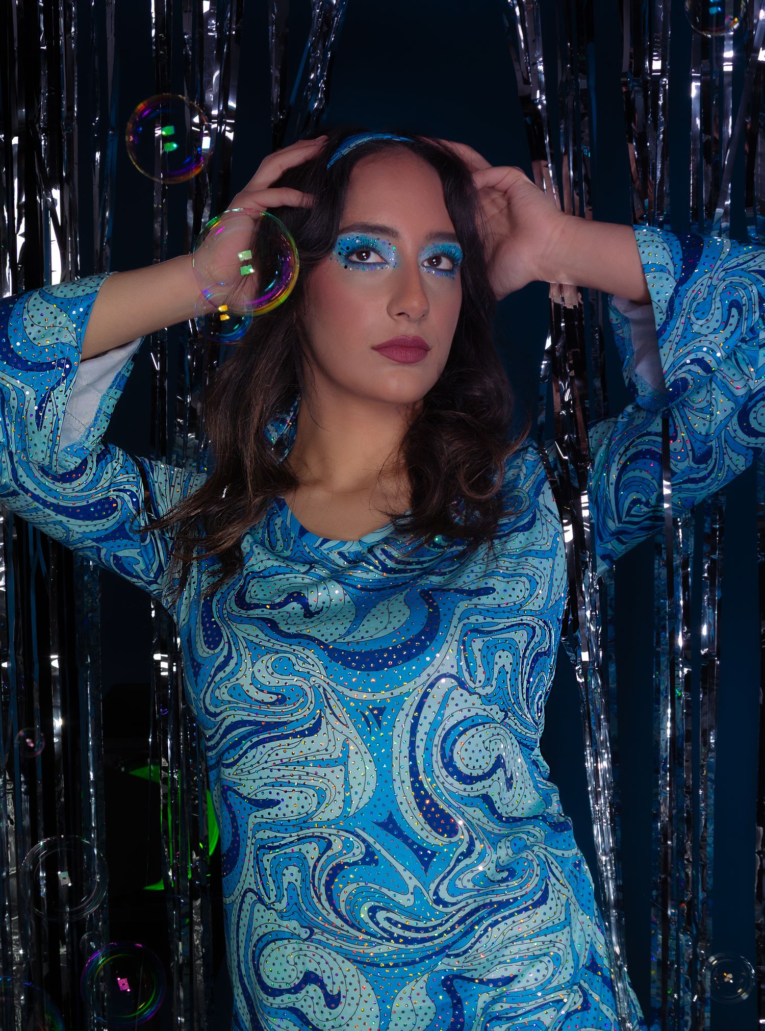 Girl posing in front of a disco style backdrop with bubbles, hands in the air, 3/4 of body shot