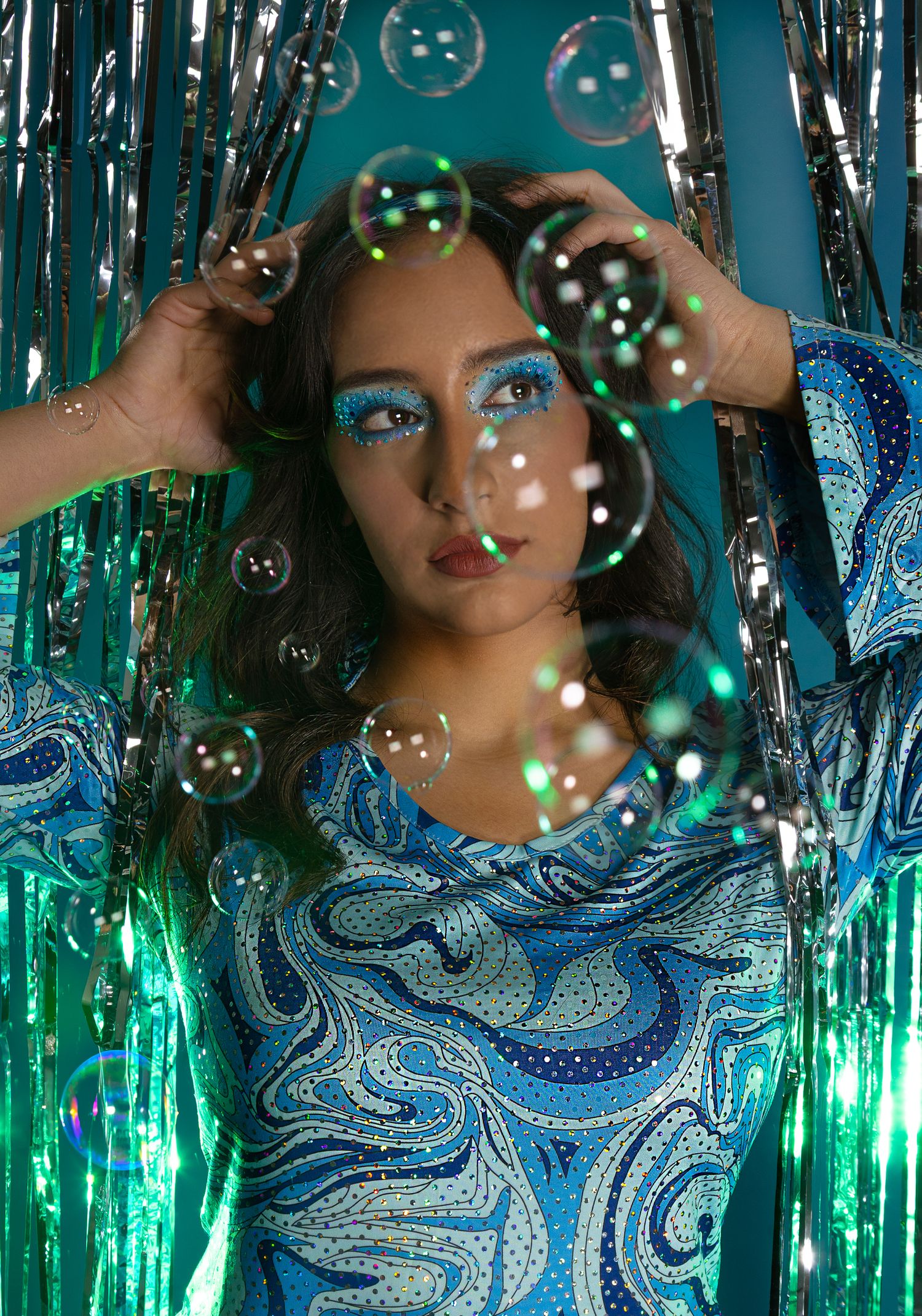 Girl posing in front of a disco style backdrop with bubbles, hands in the air, looking off to the right