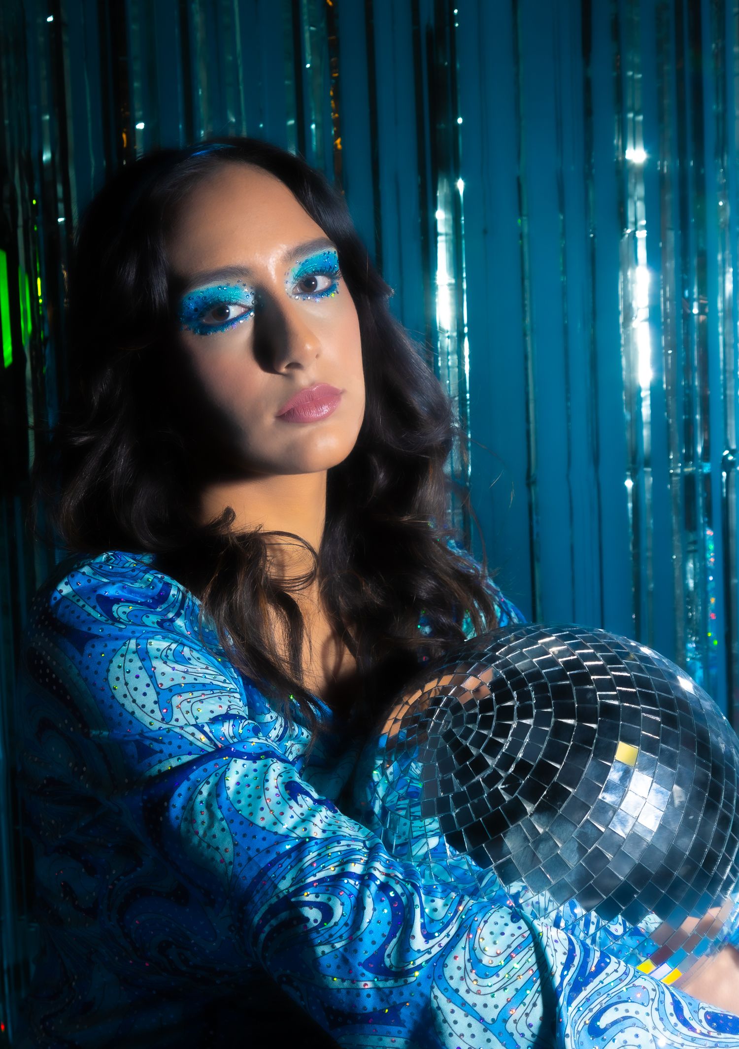 Girl sitting in front of a disco style backdrop holding a disco ball between her arms
