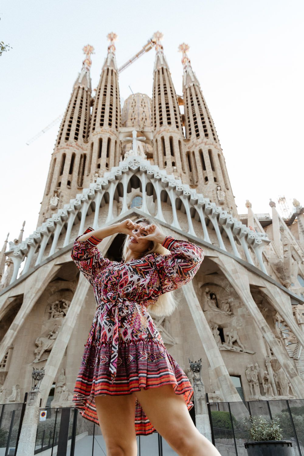 Tourist in red dress poses playfully in front of the Sagrada Familia cathedral in Barcelona.