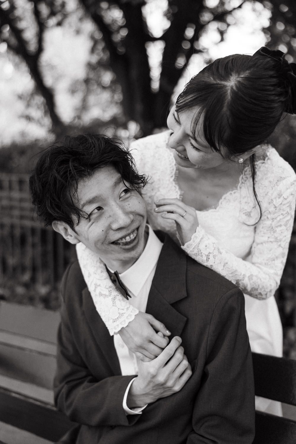 A candid black and white portrait of a couple sharing a lighthearted moment outdoors.