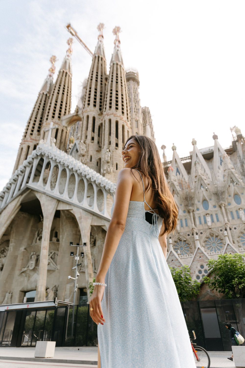 A woman in a light blue dress poses in front of the iconic Sagrada Familia cathedral in Barcelona.