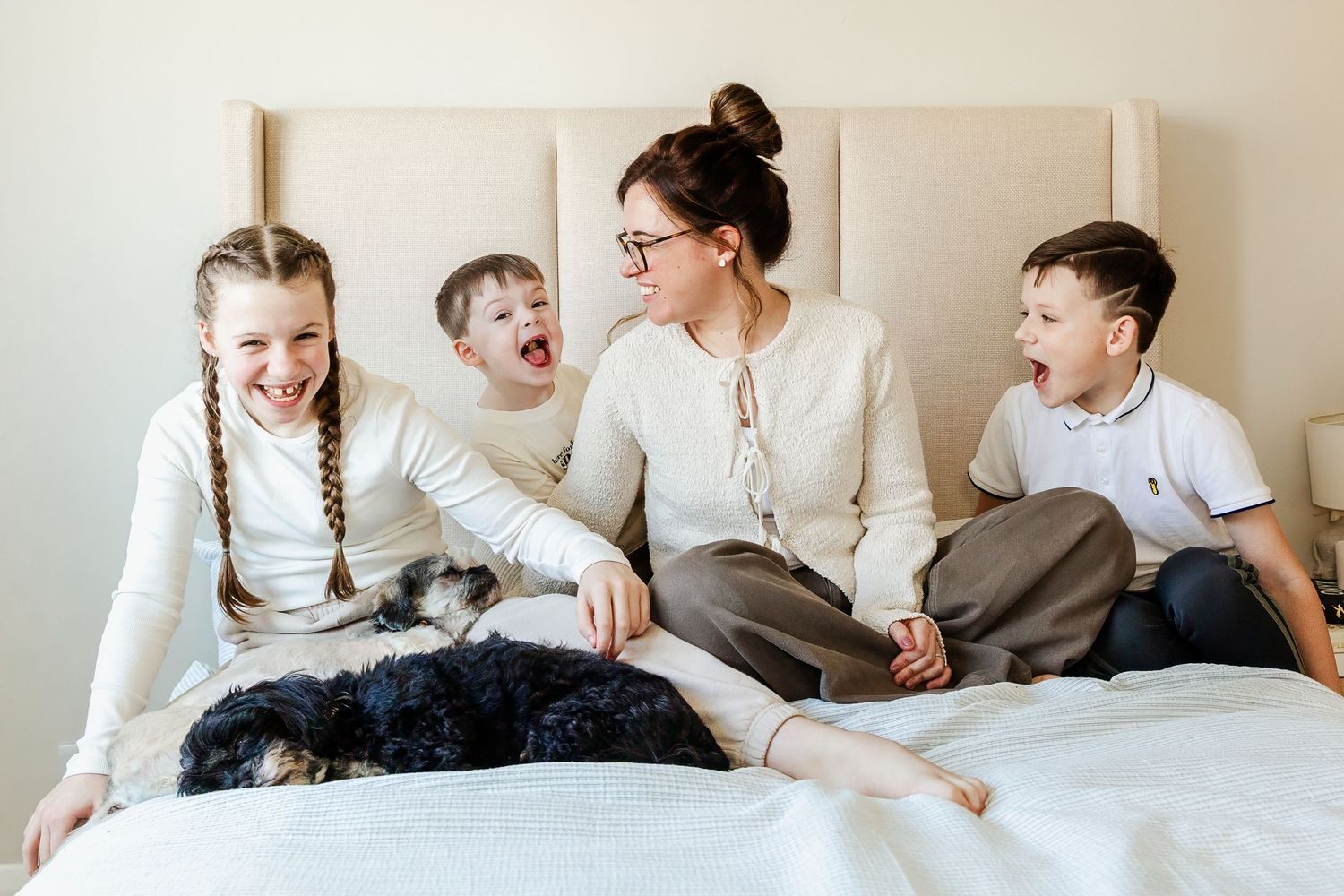 A mum sits on her bed at home with her three children and their pet dog. They looked relaxed as they smile and play. Bristol family photos