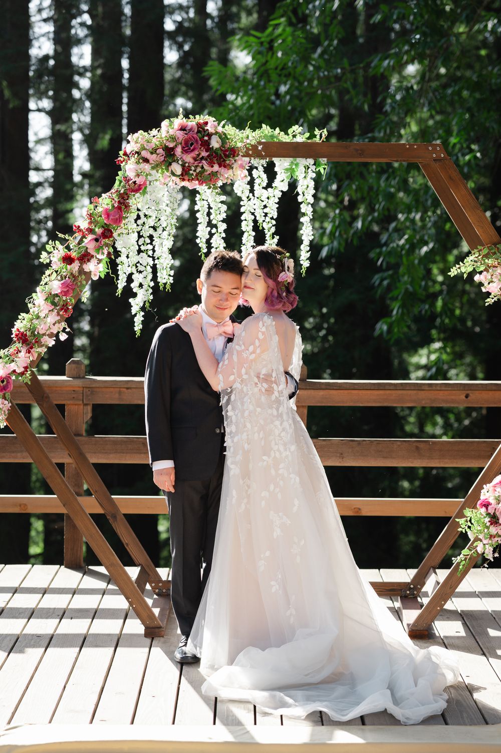 Wedding ceremony setup in a forest with wooden arch decorated with cascading pink and white floral arrangements.