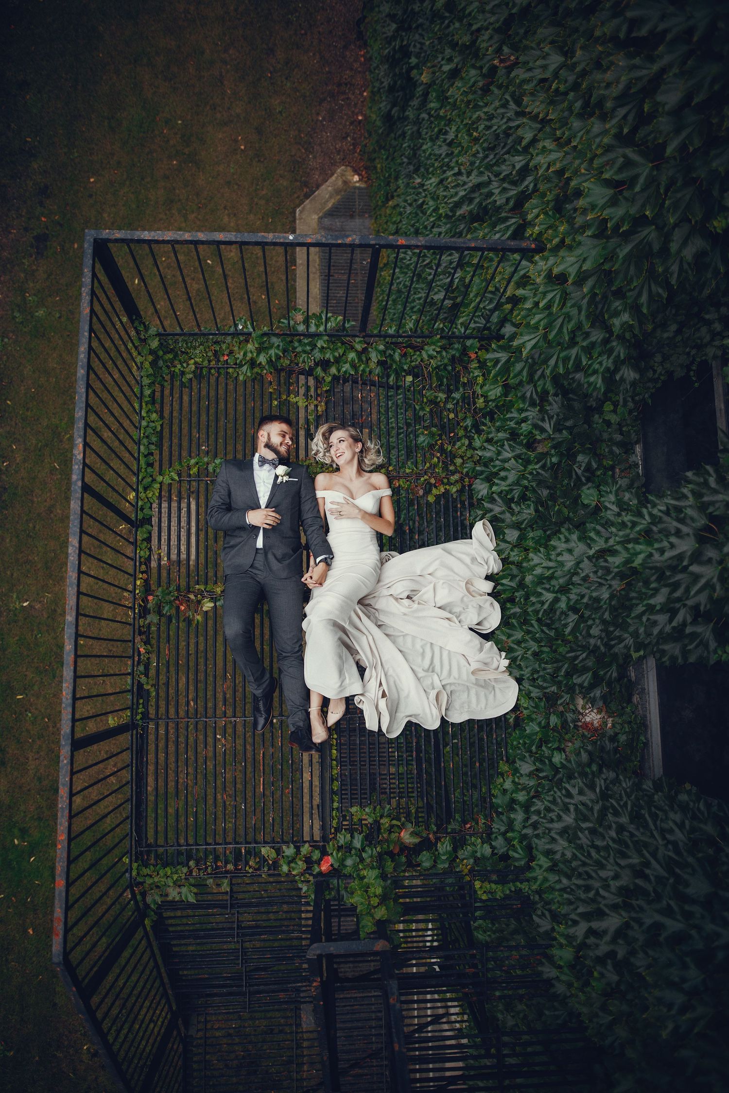 A romantic couple shares an intimate kiss while holding a decorative lace fan in a moody outdoor setting.
