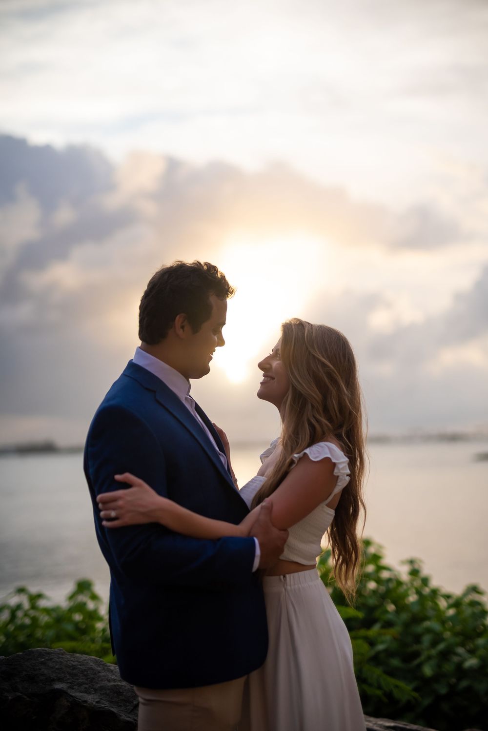 A romantic couple embraces on a cliff at sunset with an ocean view, creating a silhouette against the glowing sky.