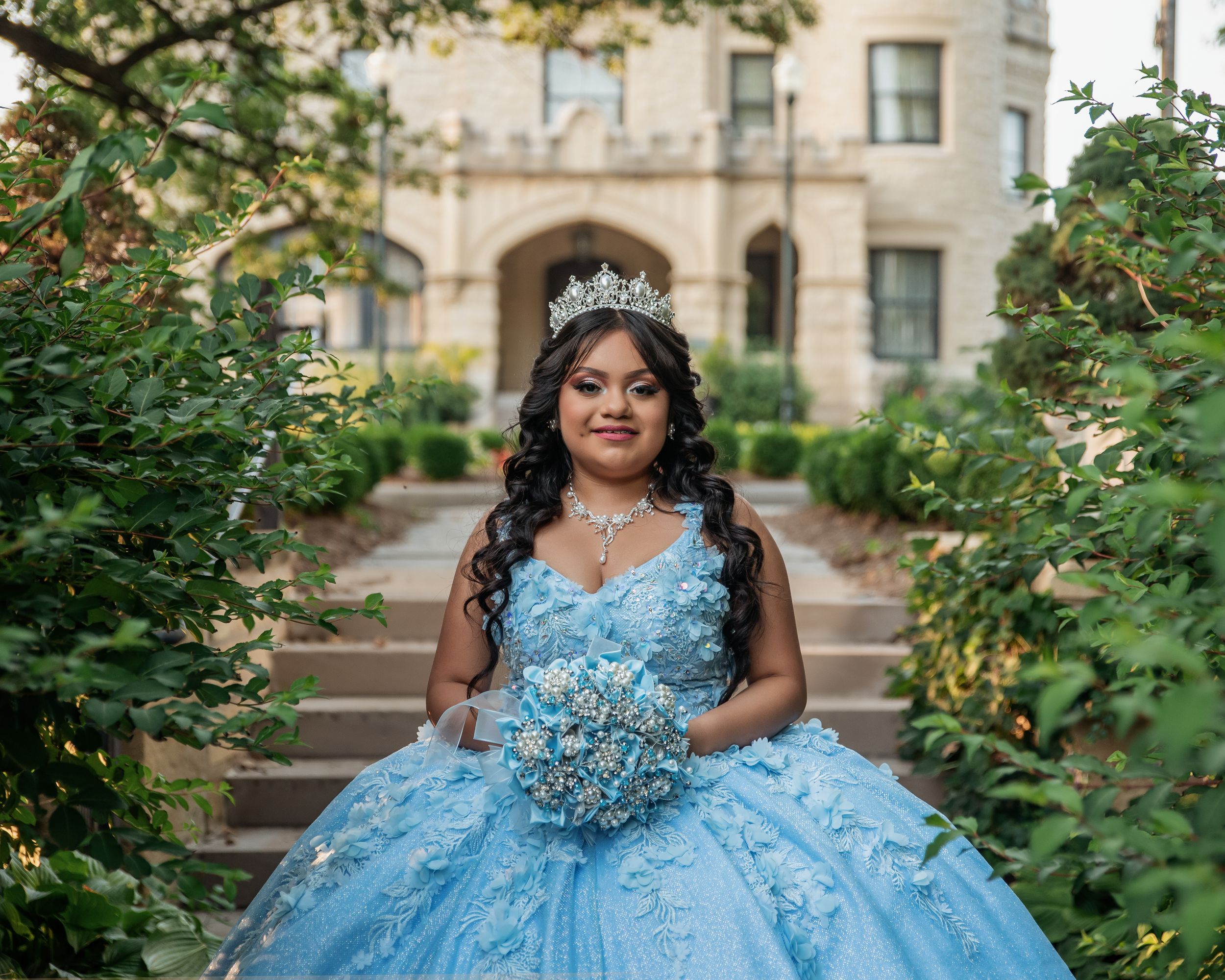 A stunning light blue ballgown with intricate beading photographed in an outdoor garden setting.