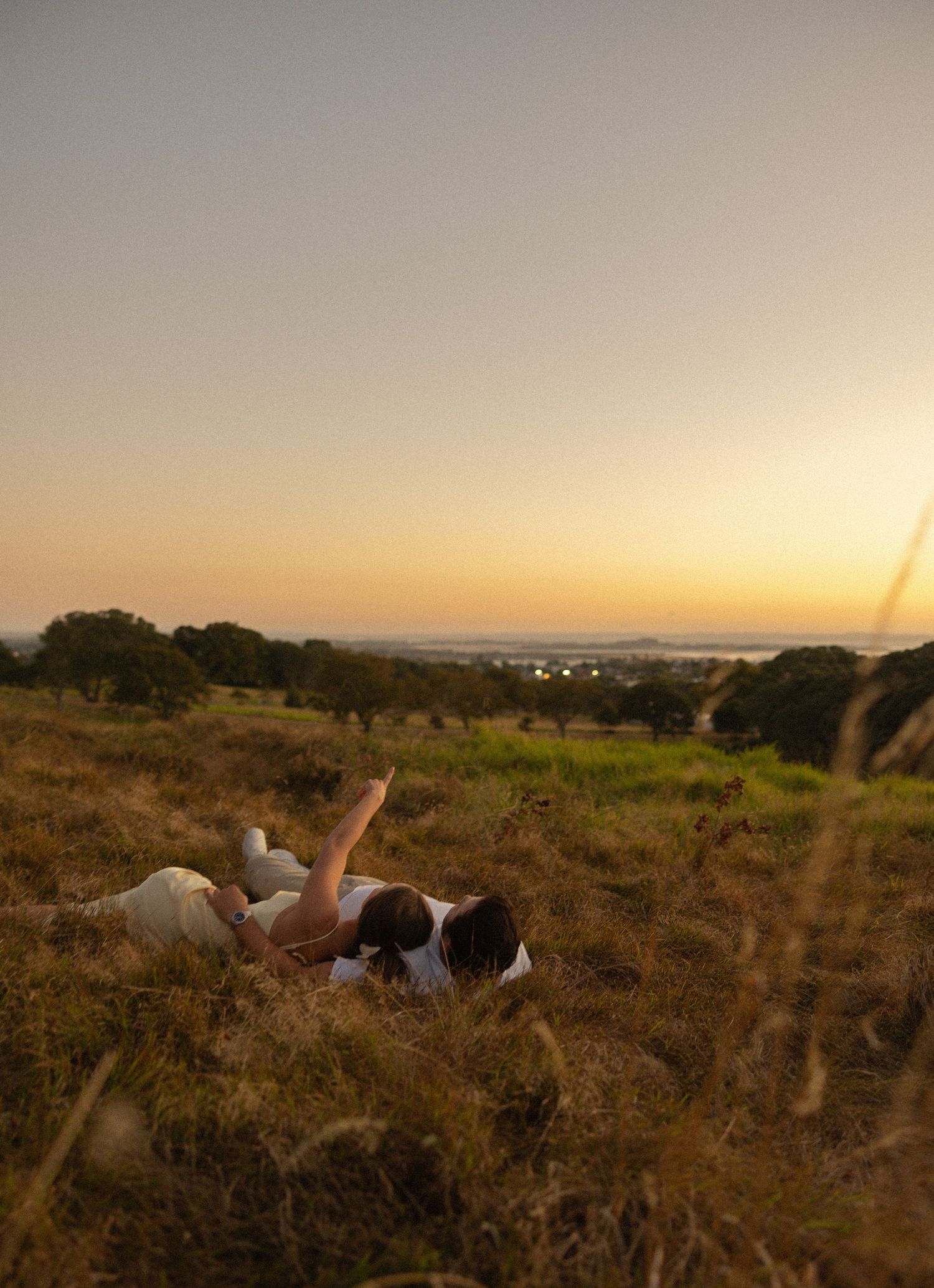 A couple stands in a golden field at dusk with the moon visible in the dusky sky.