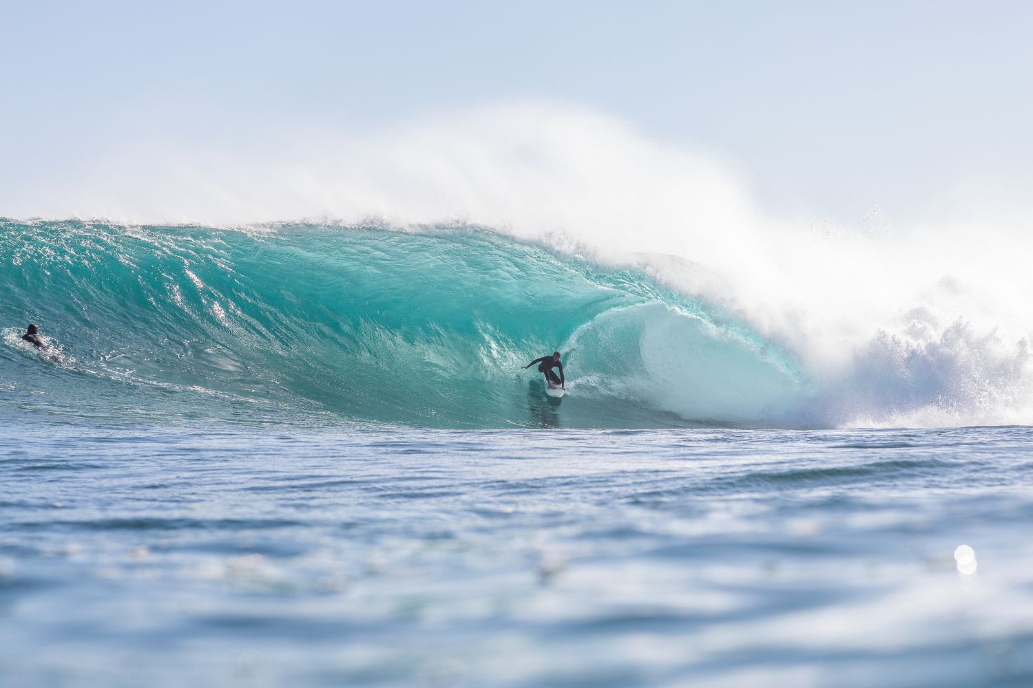 A surfer rides inside a large turquoise wave barrel breaking in the ocean.