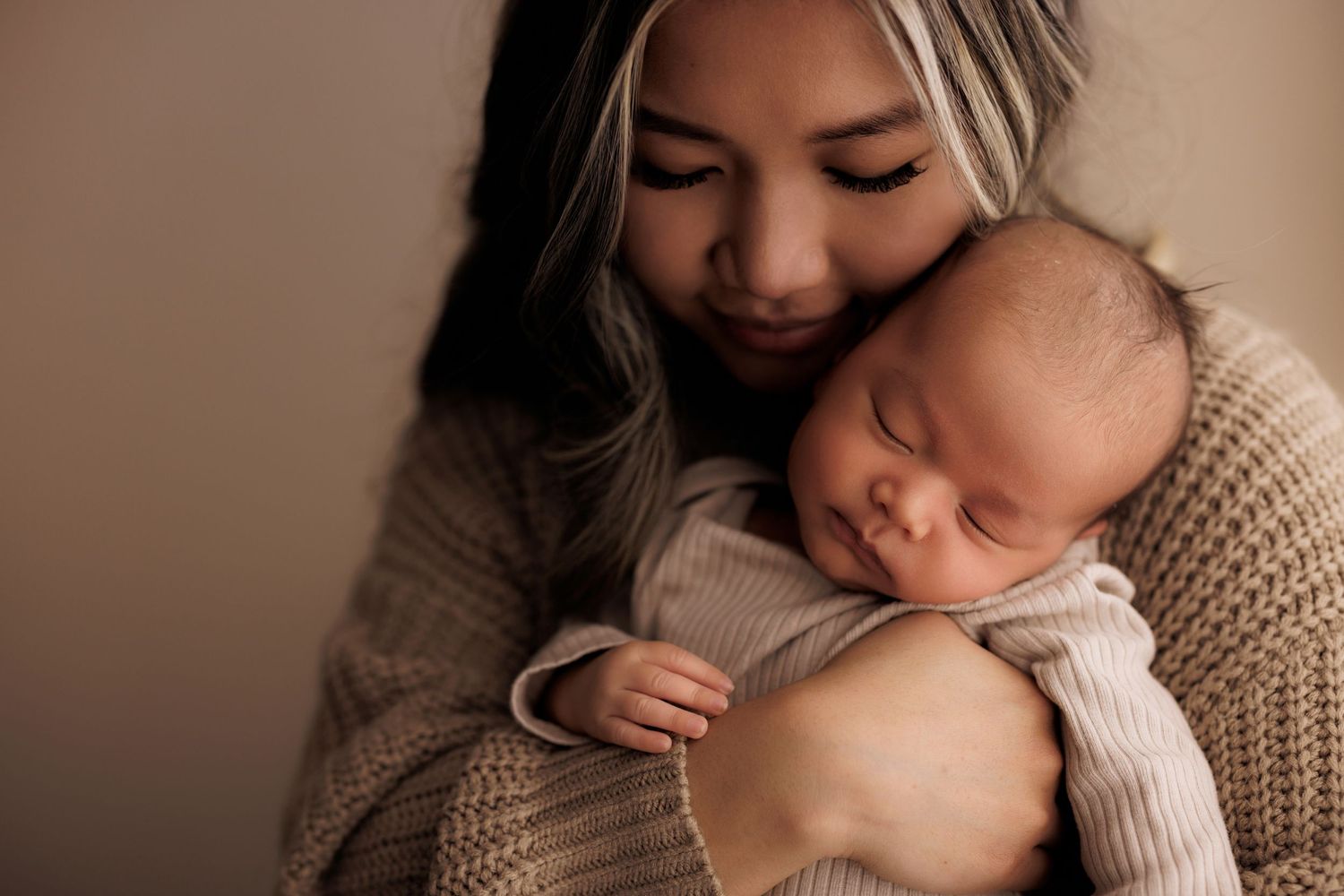 A sleeping baby rests peacefully in a knit sweater while being cradled in warm, gentle embrace by caregiver.