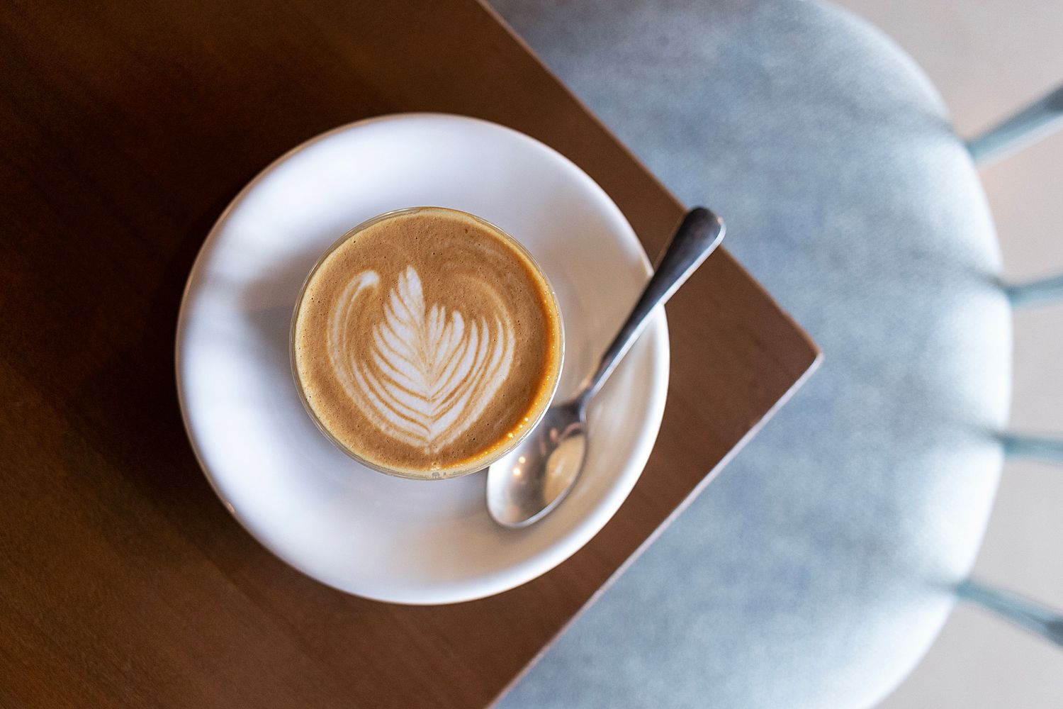 Overhead view of lcortado with rosetta-shaped foam art on white saucer with spoon.