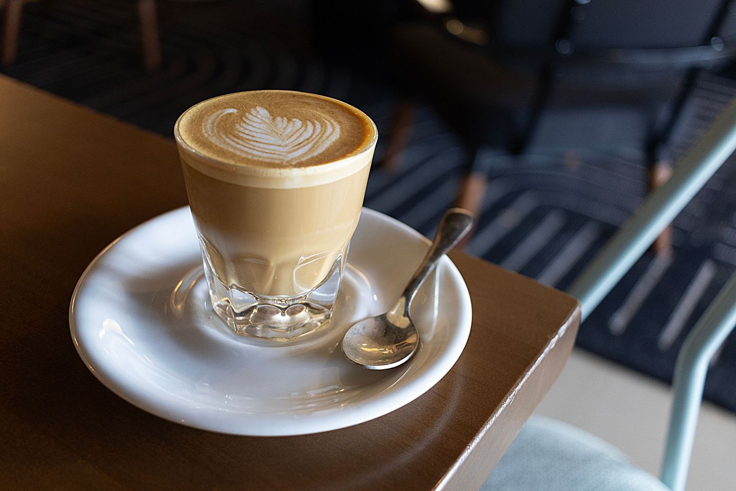 Cortado with artistic foam design served in clear glass on white saucer.