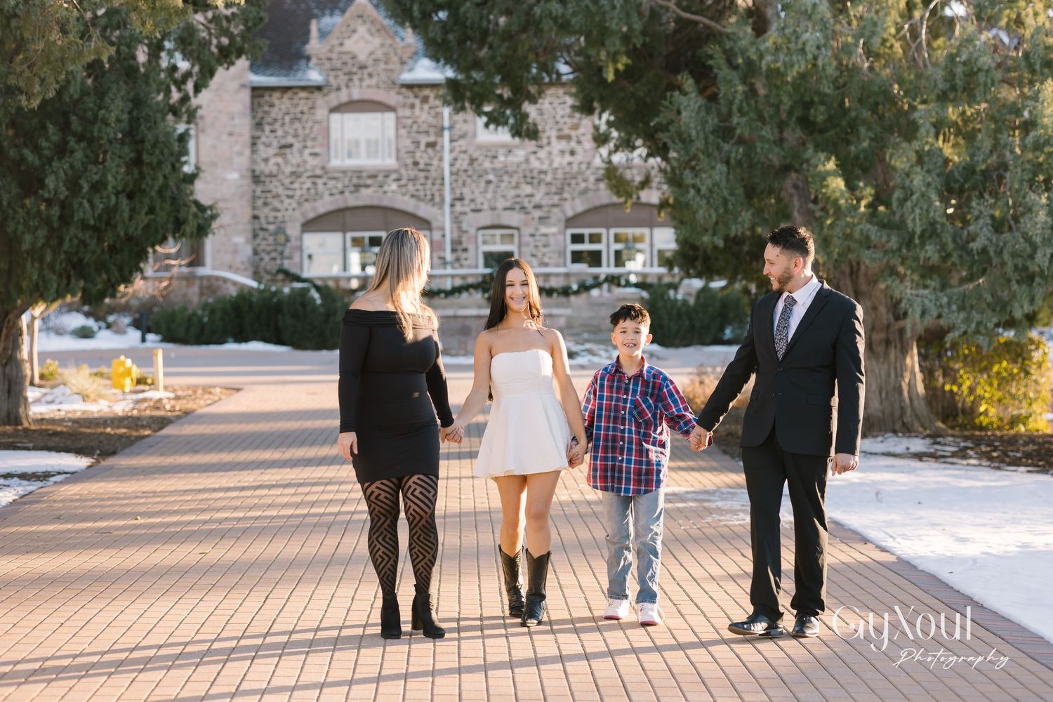 A group walks together holding hands on a stone path in front of a large stone house during sunset.
