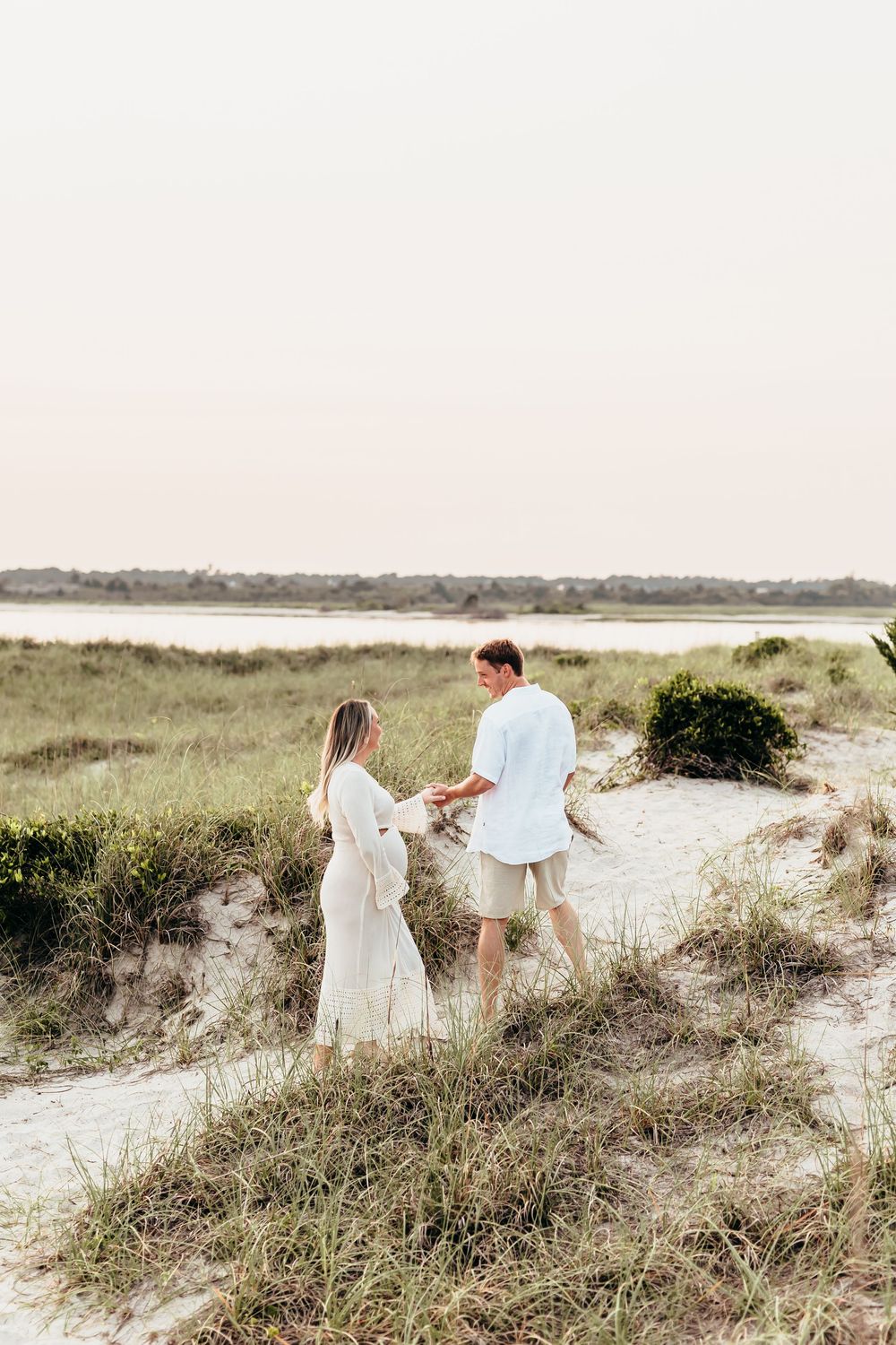 Couple explores sandy coastal dunes during golden hour photography session.Sunset Wrightsville beach wilmington nc