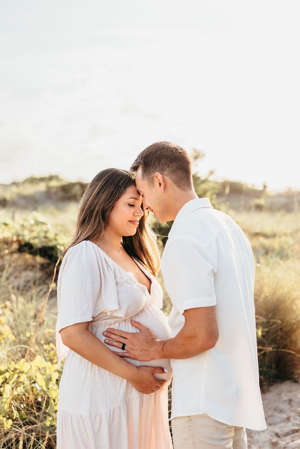 A tender moment between a couple in white outfits on a beach at sunset.
