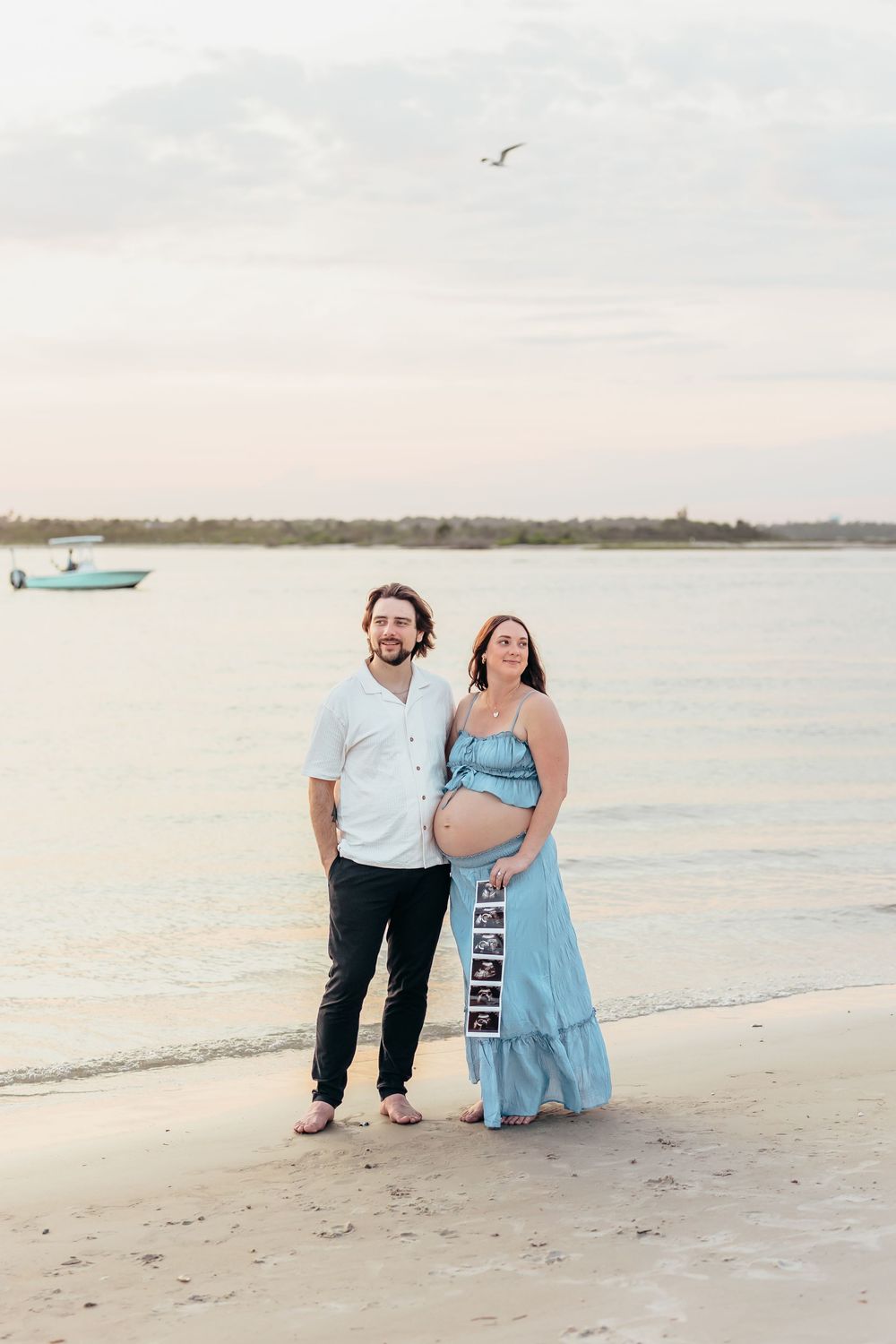 Couple holds ultrasound photo while walking along peaceful beach shore. Sunset Wrightsville beach wilmington nc