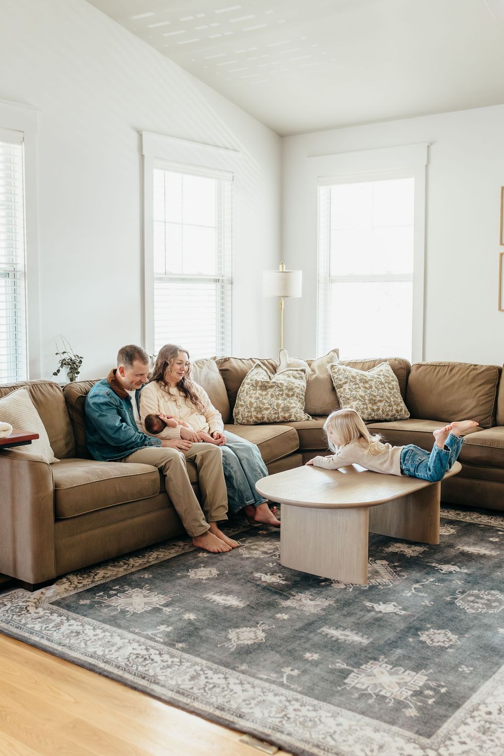 Family relaxing on a large brown sectional sofa in a bright, cozy living room with a modern coffee table.