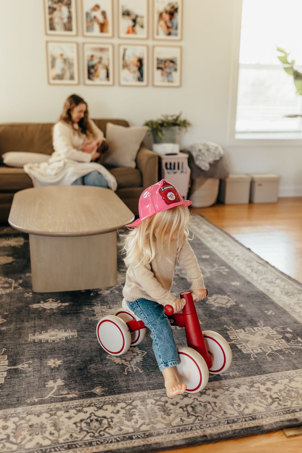 A child plays and crawls on a large gray patterned area rug in a bright living room with wall art.