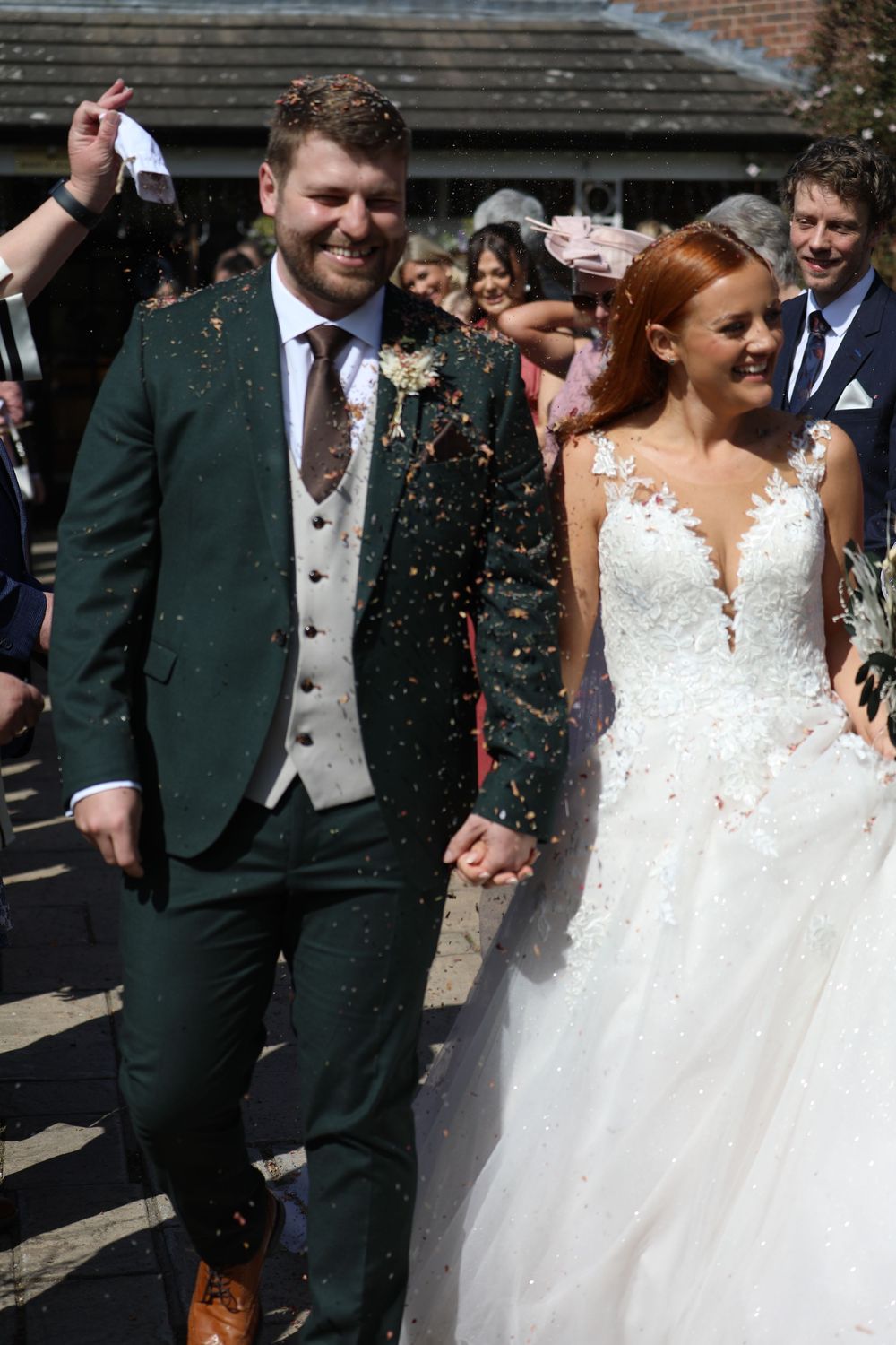 Newlyweds walk through shower of confetti while guests celebrate their wedding day.