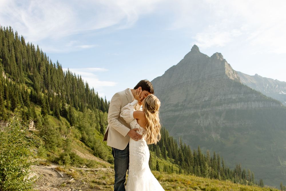 Romantic couple embraces on mountain trail with majestic peak and evergreen forest in background.
