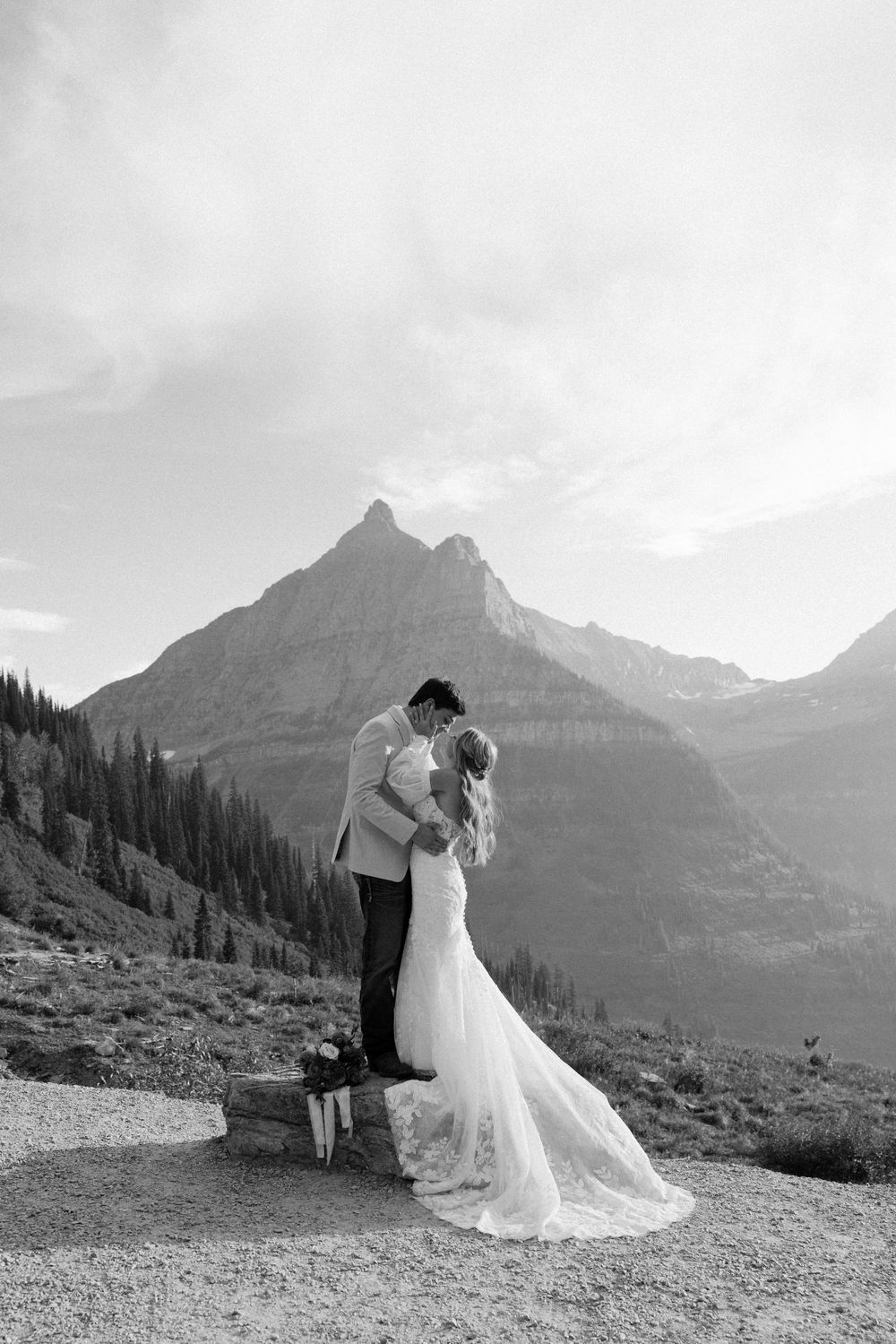 A romantic wedding couple shares an intimate moment against the dramatic backdrop of mountain peaks in Glacier National Park.