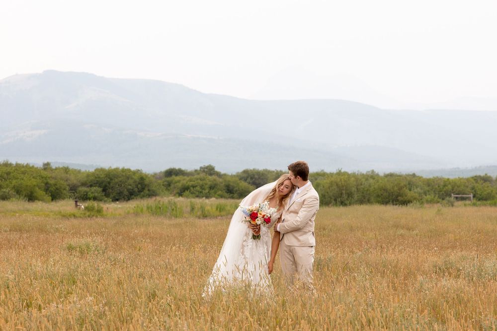 A couple shares a romantic moment in a golden meadow with misty mountains in the background.