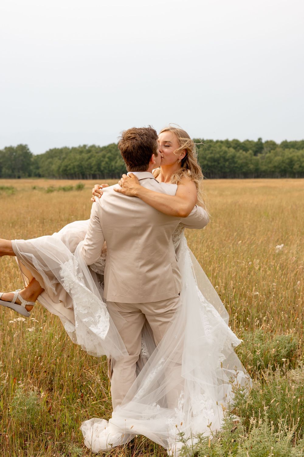A romantic wedding scene showing a couple embracing and dancing in a golden summer field with flowing white dress.