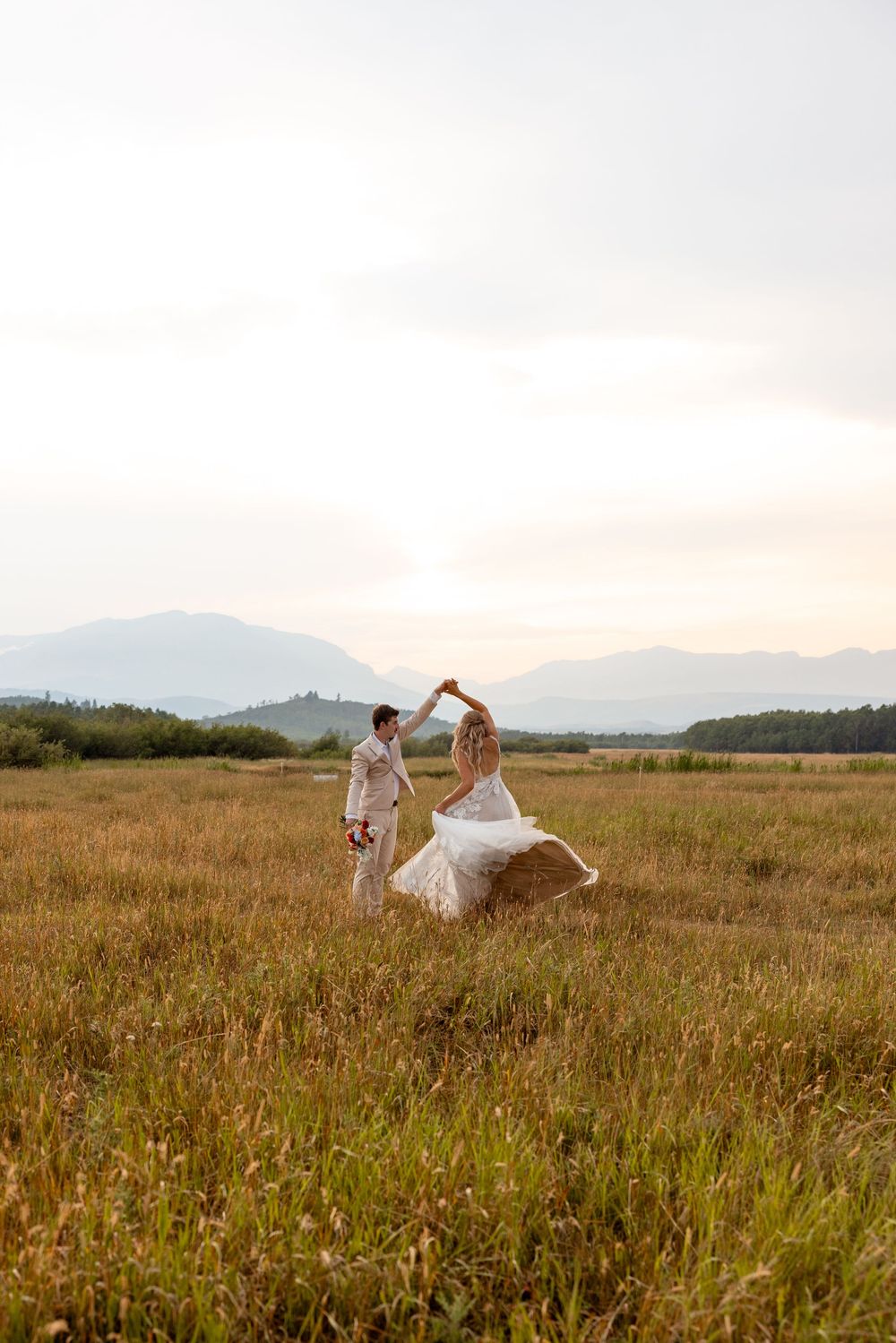 Newlyweds dance and twirl joyfully in a golden mountain meadow at sunset.