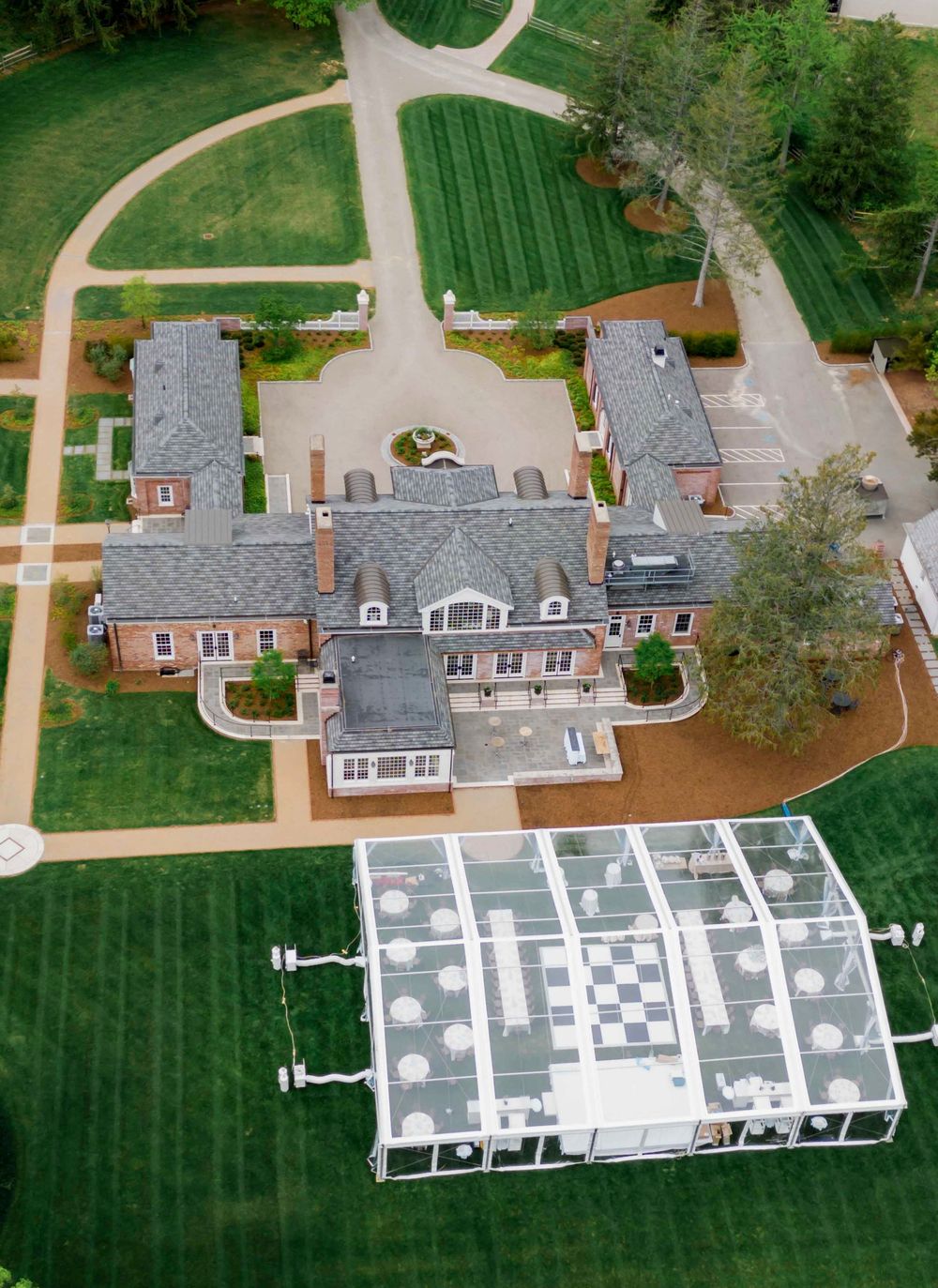 Aerial view of a classic estate with grey roofs and manicured lawns showing architectural paths and modern glass structures.