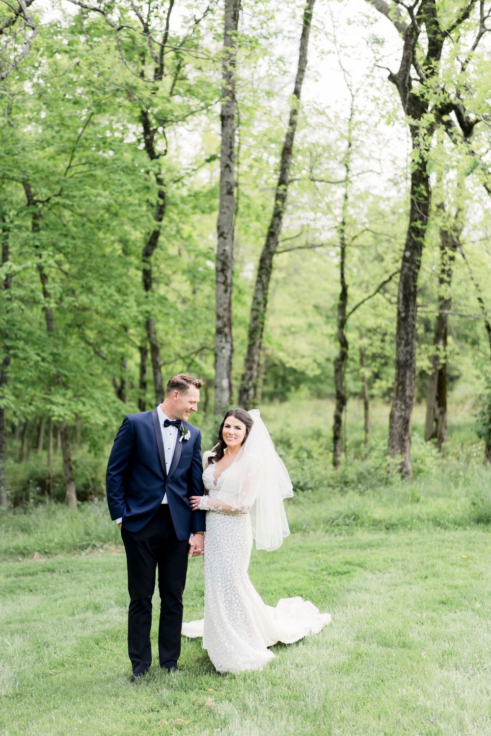 A romantic wedding moment in a lush green forest setting with a white lace gown and classic tuxedo.
