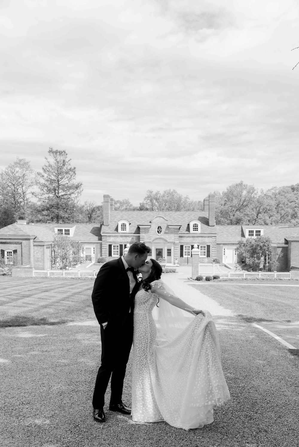 A couple shares a romantic moment on a lawn with a stately house in the background on their wedding day.