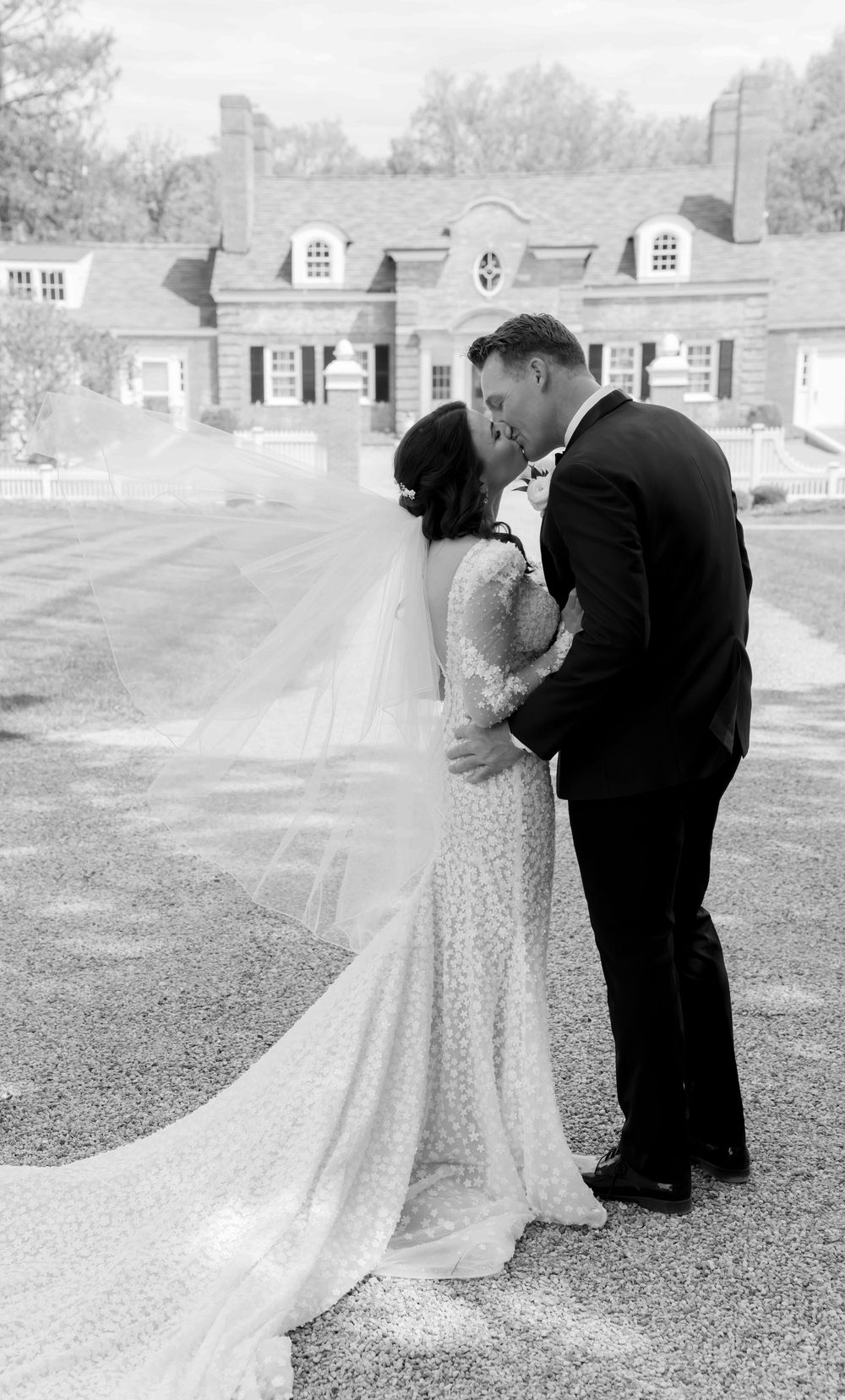 A romantic black and white wedding moment set against a classic colonial style house.