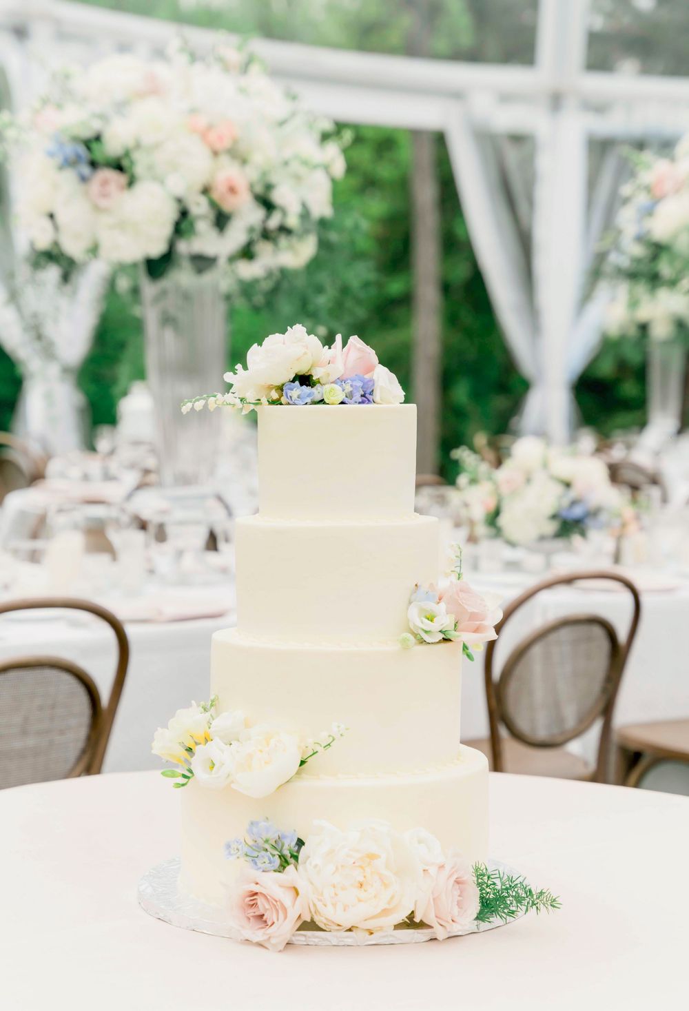 Classic white tiered wedding cake adorned with blush roses and blue accents on table with floral reception decor.