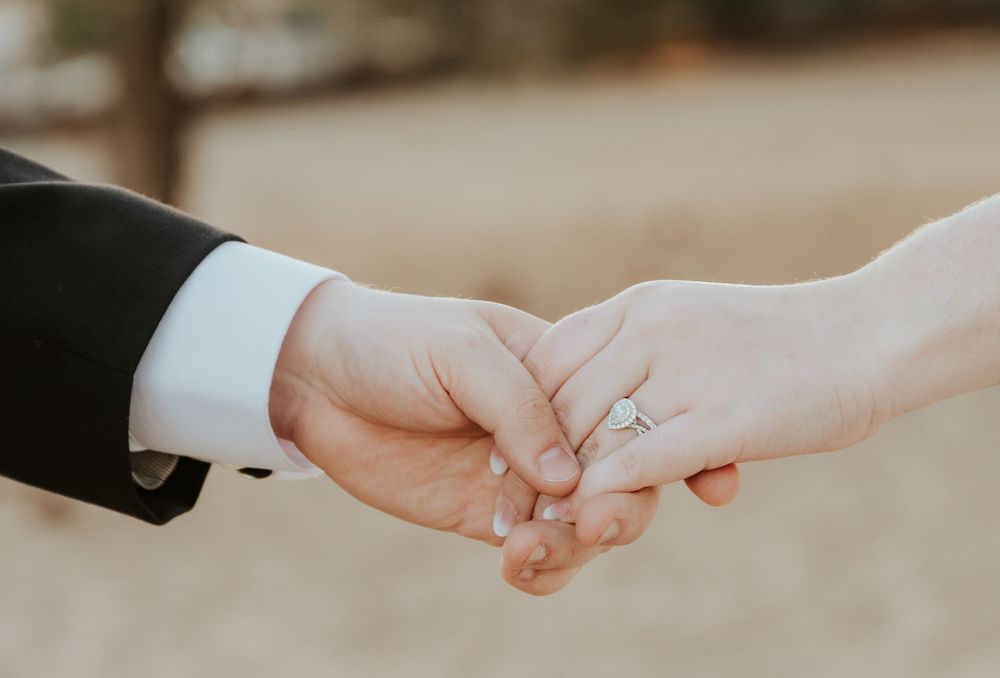 Close-up view of hands wearing wedding rings in soft daylight, with bride in white& groom in black sleeves wedding Tahoe, Reno photographer