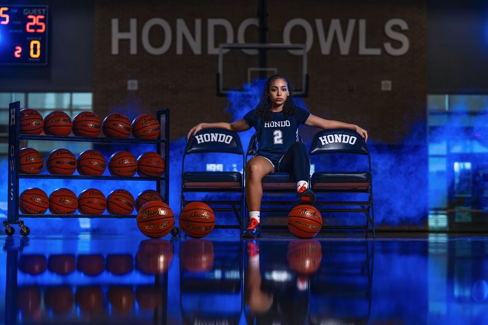 A basketball scoreboard displays HONDO OWLS against a blue background with sports equipment visible in the background.