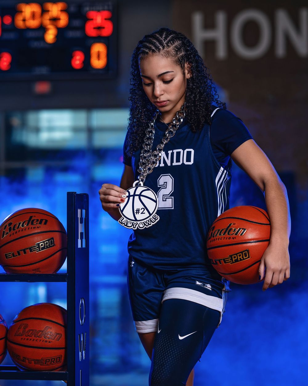 Basketball player in Orlando jersey holds two basketballs while standing near rack of game balls in blue-lit environment.
