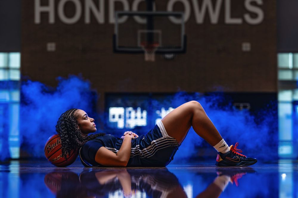 Basketball player in white jersey drives to the basket during an intense game with blue lighting effects in background.