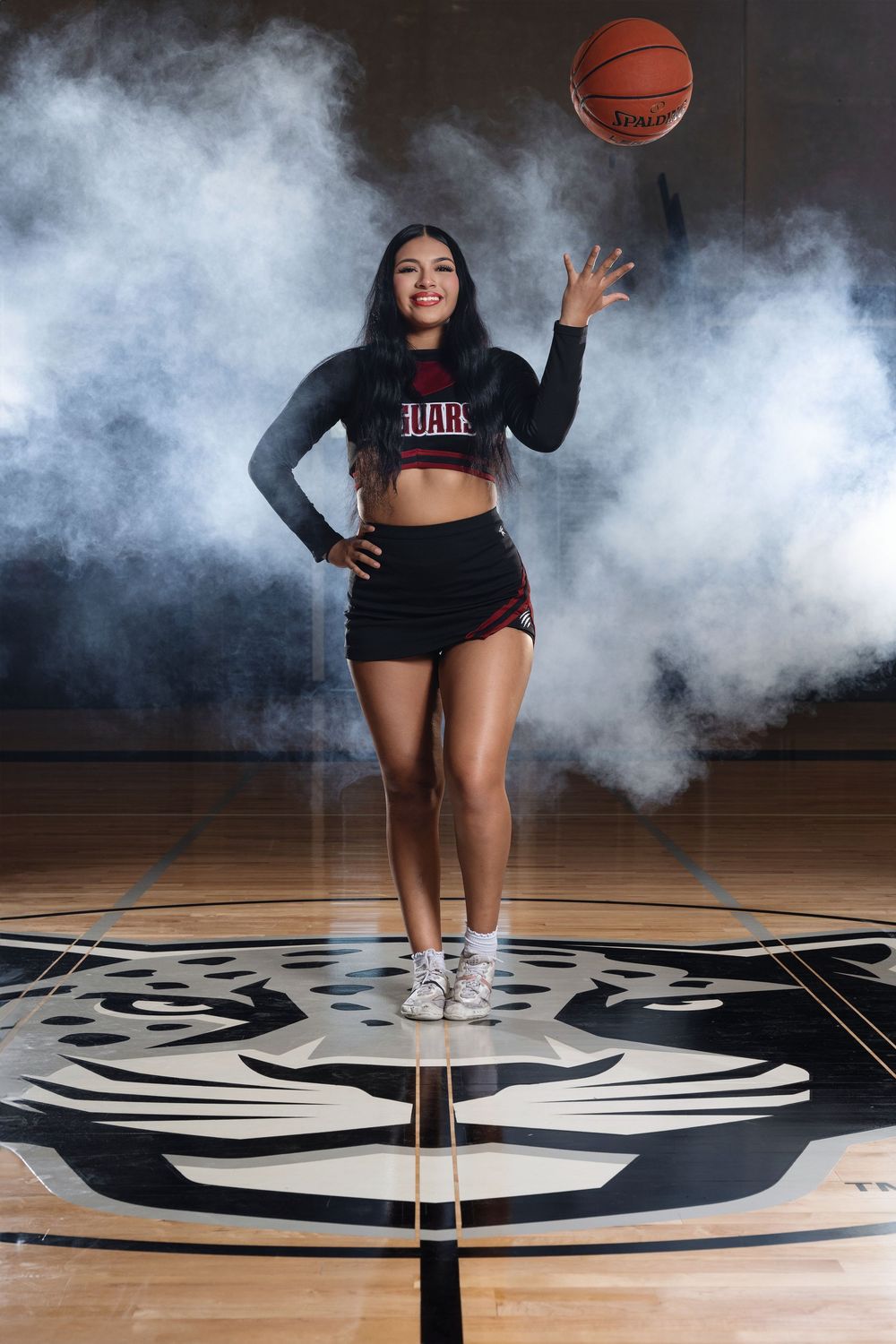 Basketball player in Dare crop top performs trick shot on wooden court with dramatic smoke effect and mascot logo background.