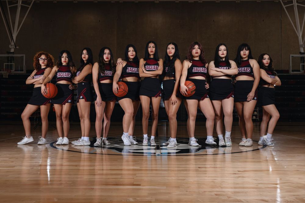 Basketball team stands in line on hardwood court holding basketballs in matching black uniforms.