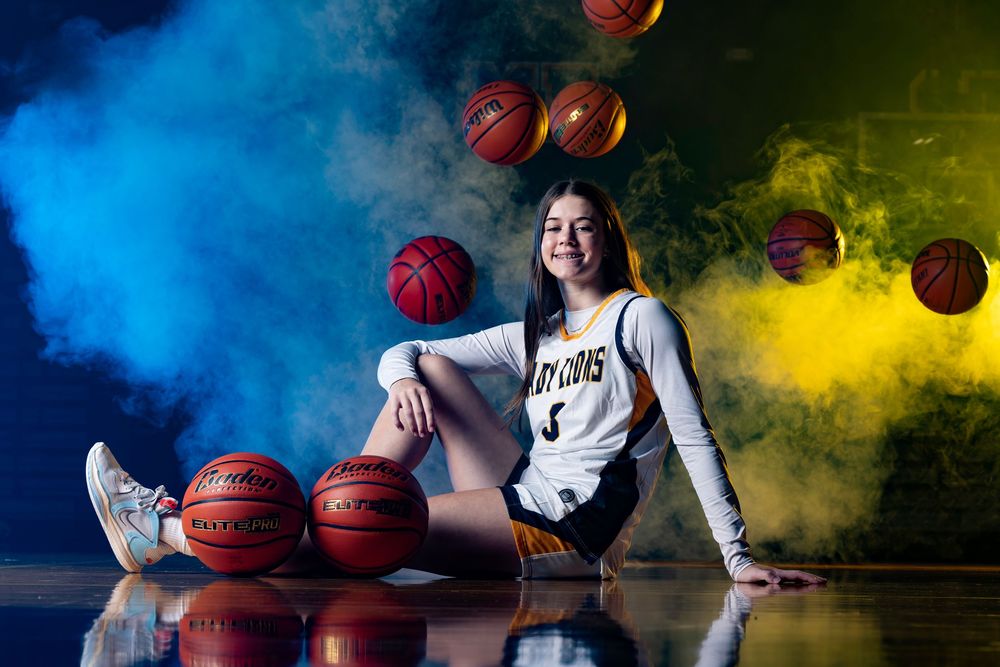 A basketball player poses with multiple basketballs against dramatic blue and yellow smoke backdrop.