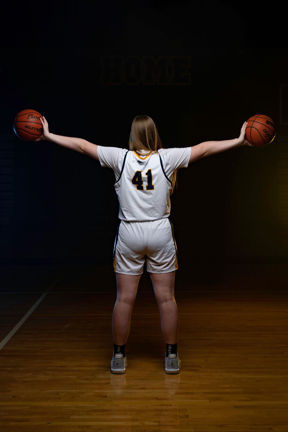 Basketball player in white uniform number 41 stands on court holding two basketballs with arms outstretched.
