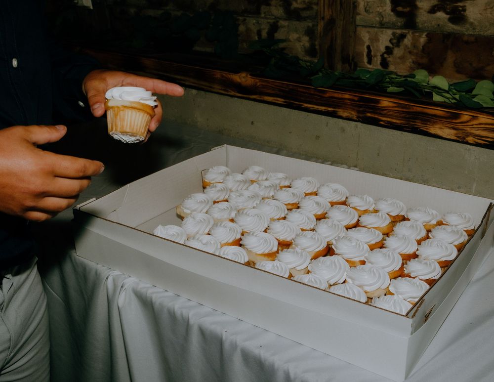 A hand reaches for a cup of coffee next to a tray filled with powdered sugar-covered Italian wedding cookies on a white tablecloth.