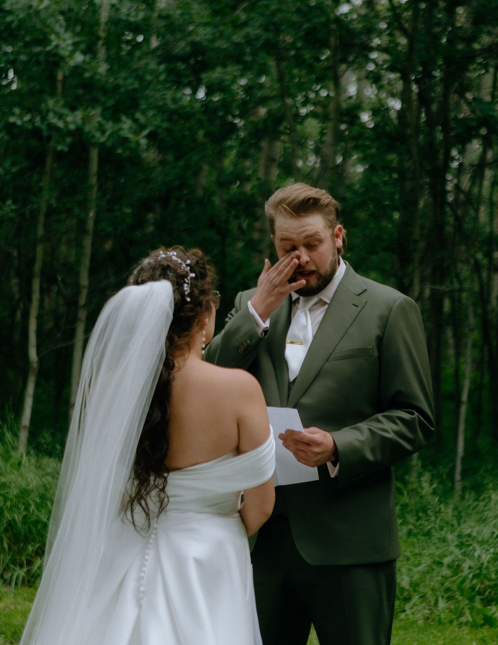 An emotional moment during a wedding ceremony in a lush forest setting as vows are being read between the couple.