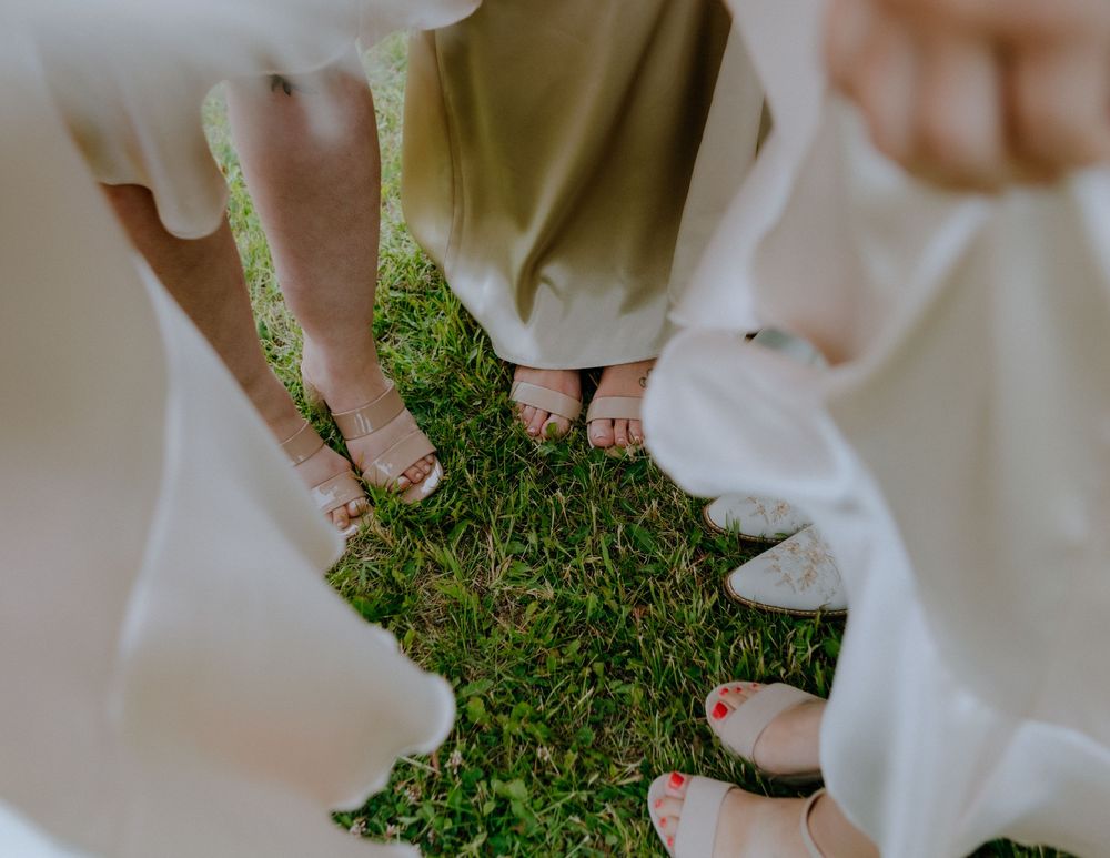 Two sets of bare feet stand intimately on grass together, dressed in flowing white garments.