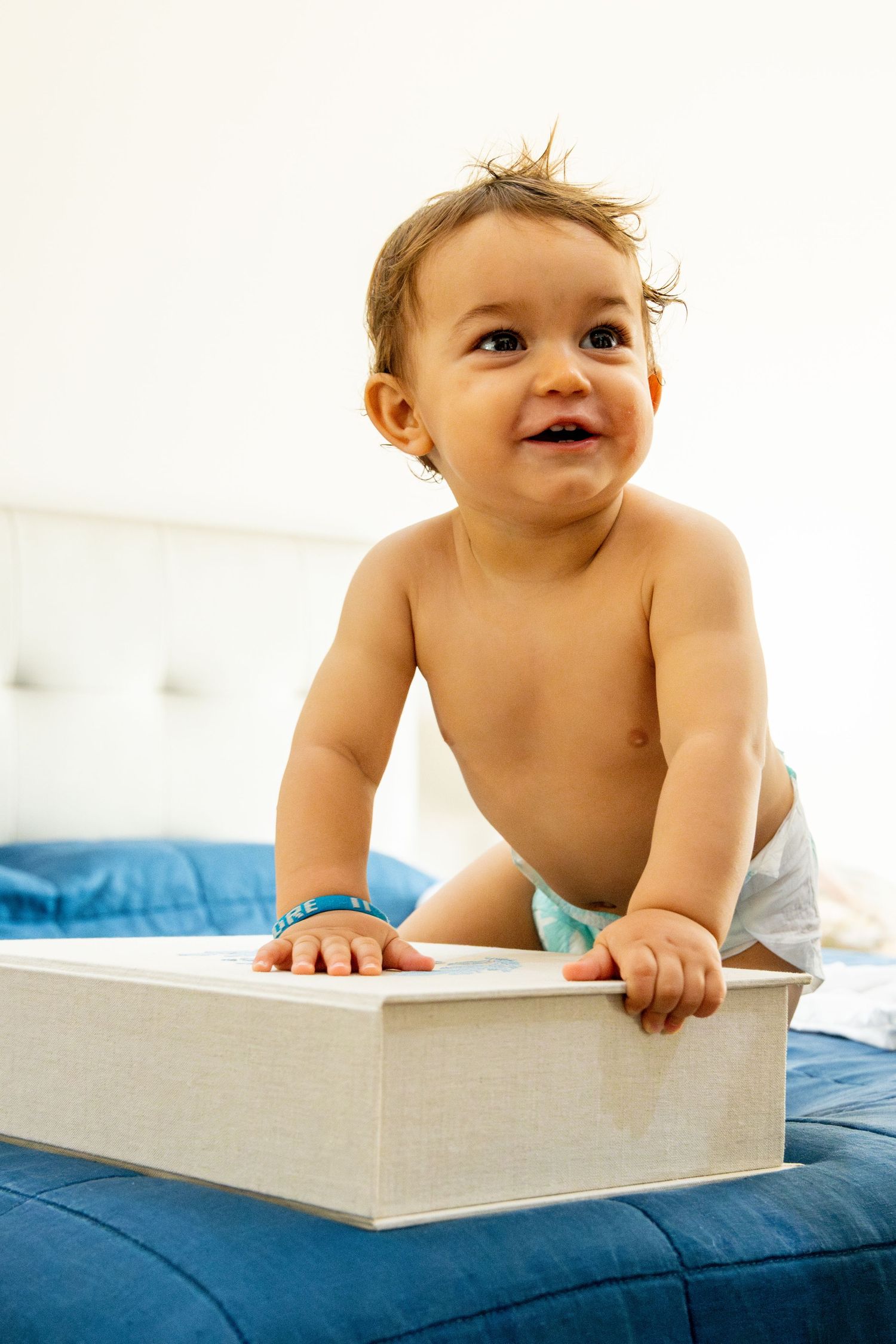 Happy baby crawling on blue bedding while reaching for a white box.