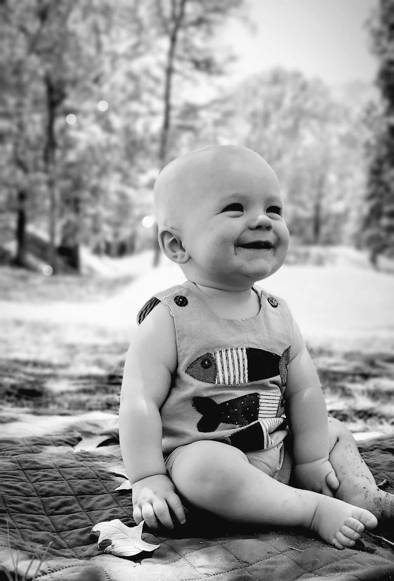 baby boy in an open grassy area smilingt wearing a fishy short coverall