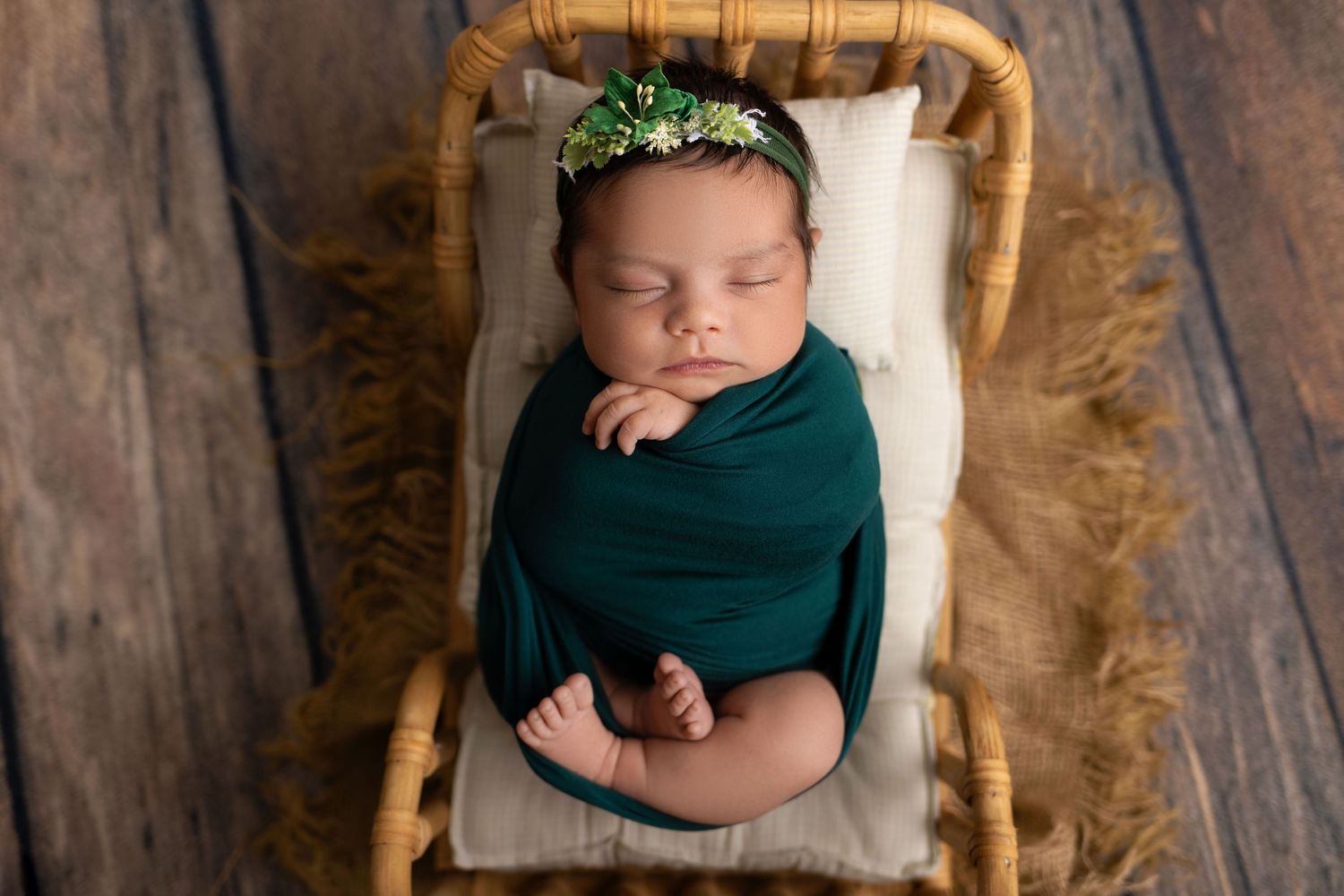 Sleeping newborn baby wrapped in teal swaddle lying on rustic wooden backdrop with natural lighting.
