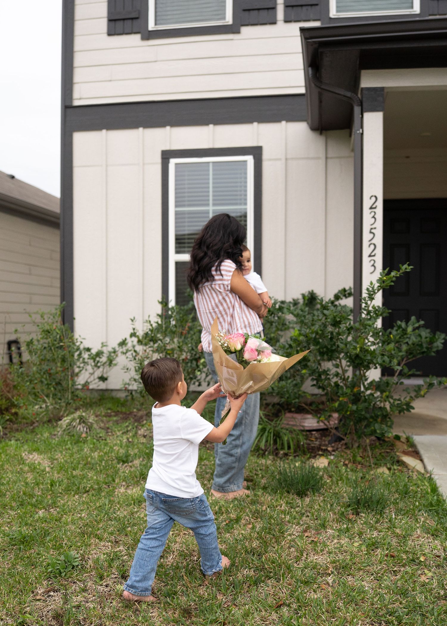 Mom holding her back turned while Dad and boys hand her the gender reveal bouquet